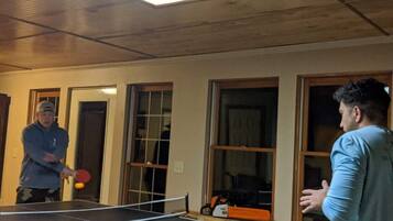 Une table de ping-pong se trouve dans une pièce aux murs en bois et aux grandes fenêtres.
