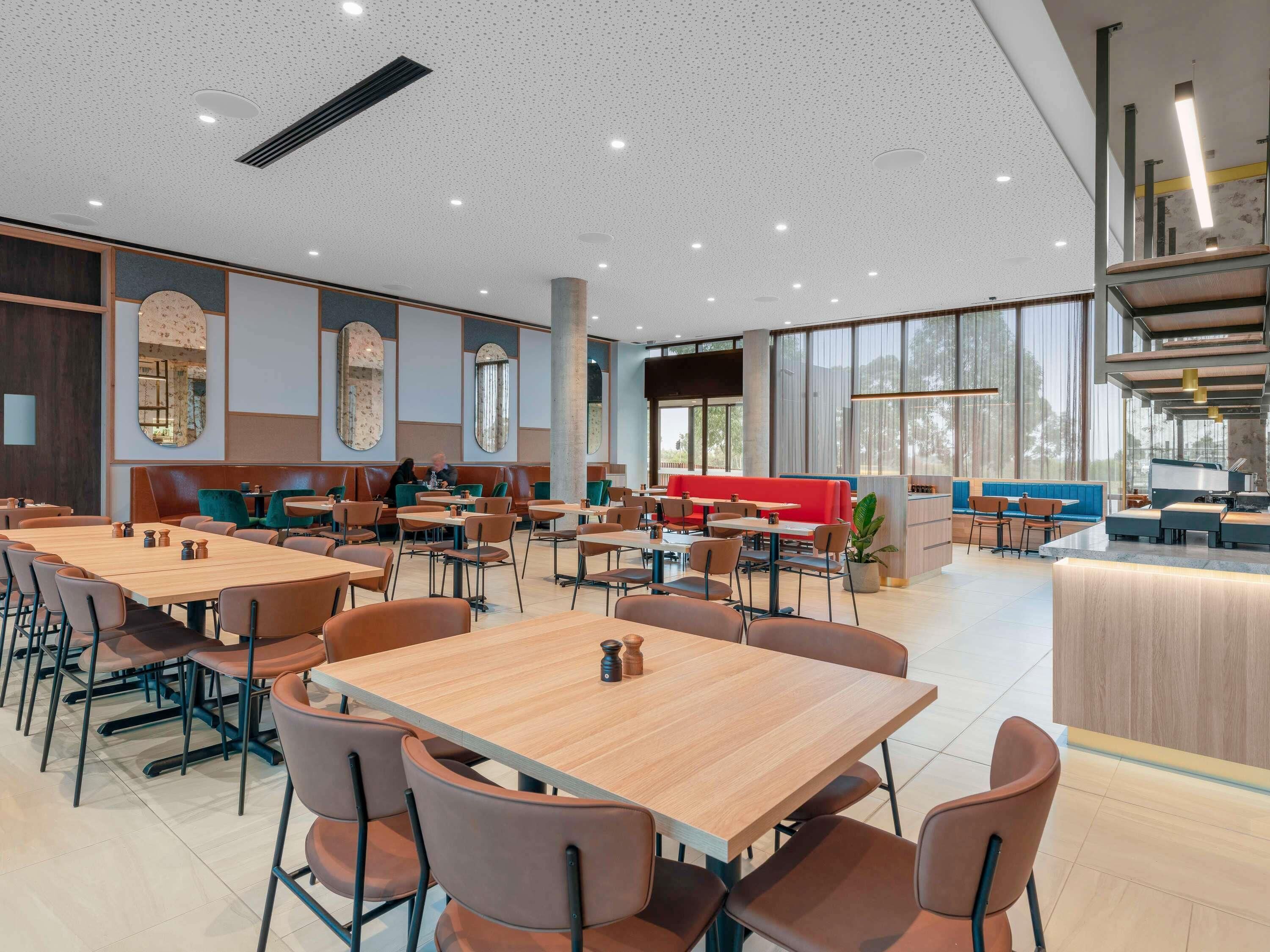 A spacious dining area with multiple tables and chairs, large windows, and a modern interior design.