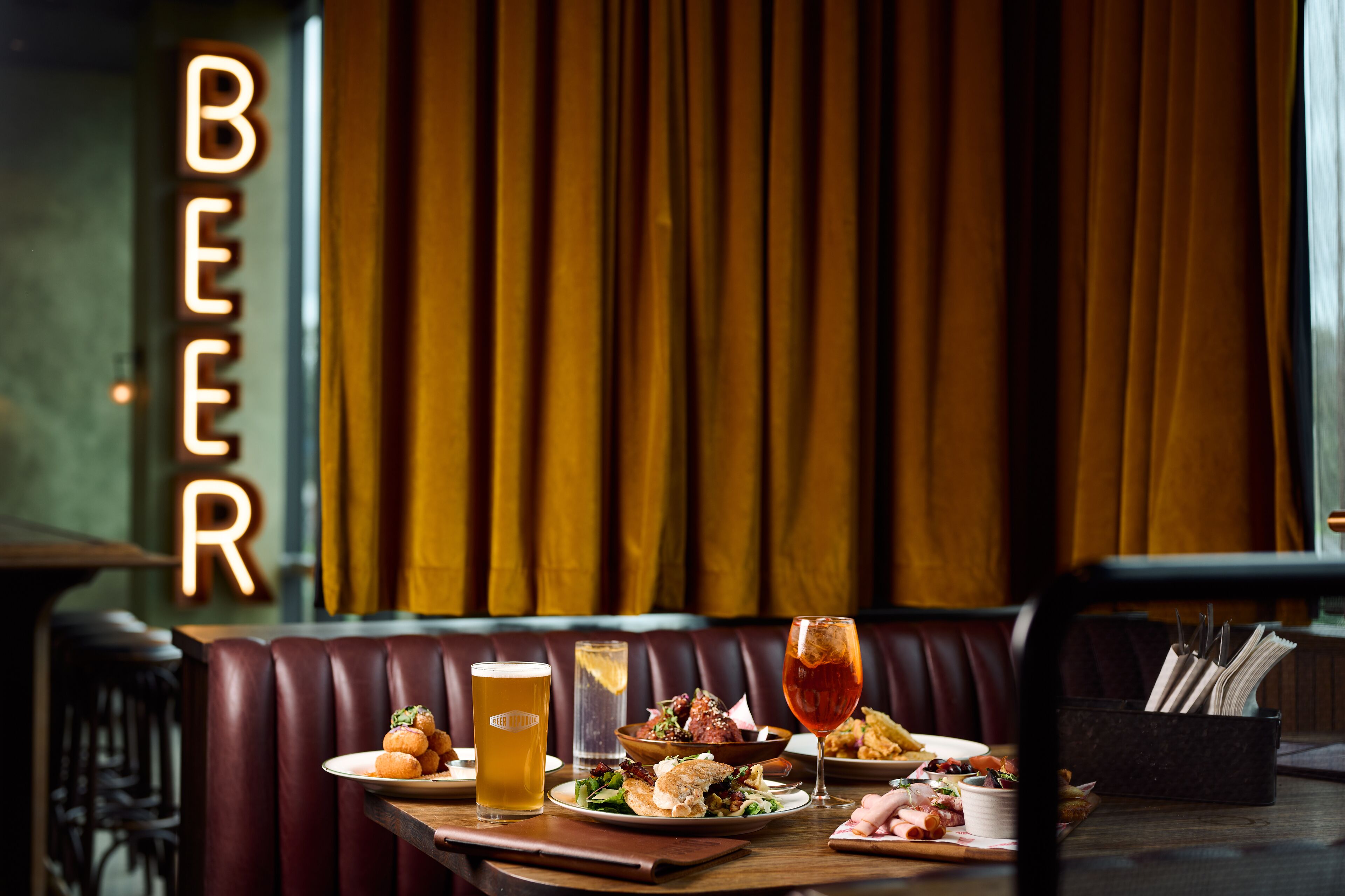 Interior de un restaurante con una mesa preparada para comer, un letrero de grifo de cerveza y vistas al exterior.