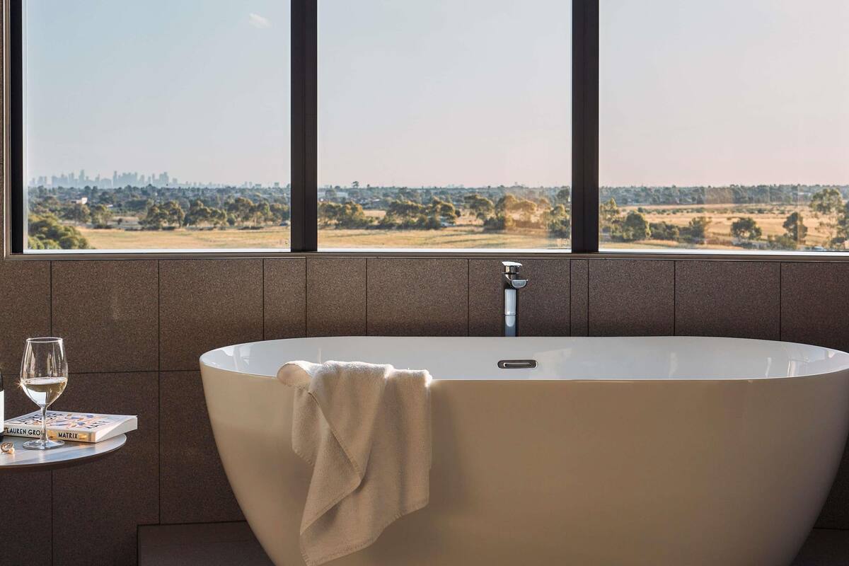 A bathroom with a freestanding bathtub, a towel, a glass of wine, and a book on a small table.