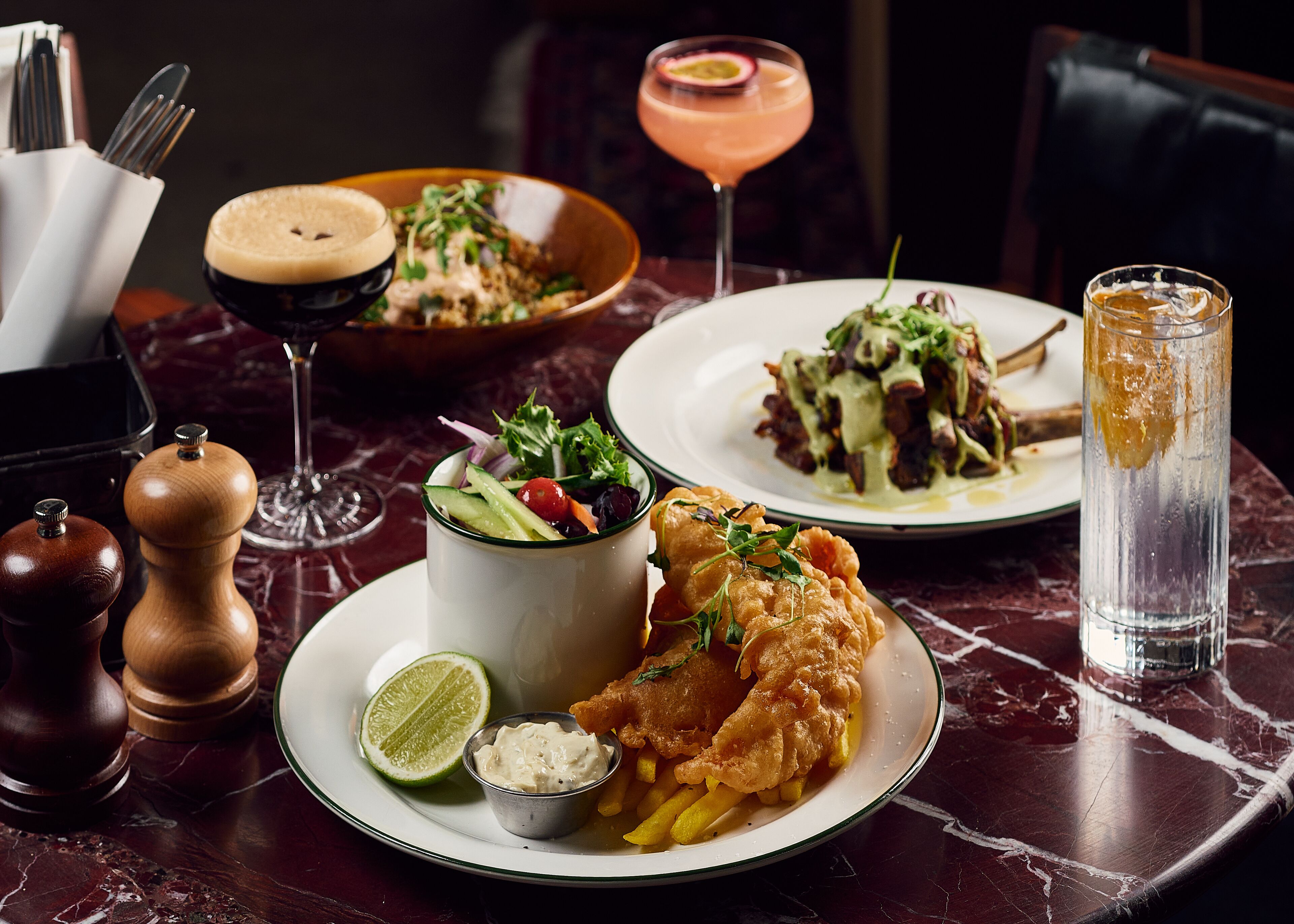 A dining table with plates of food, a cocktail, and a glass of water.