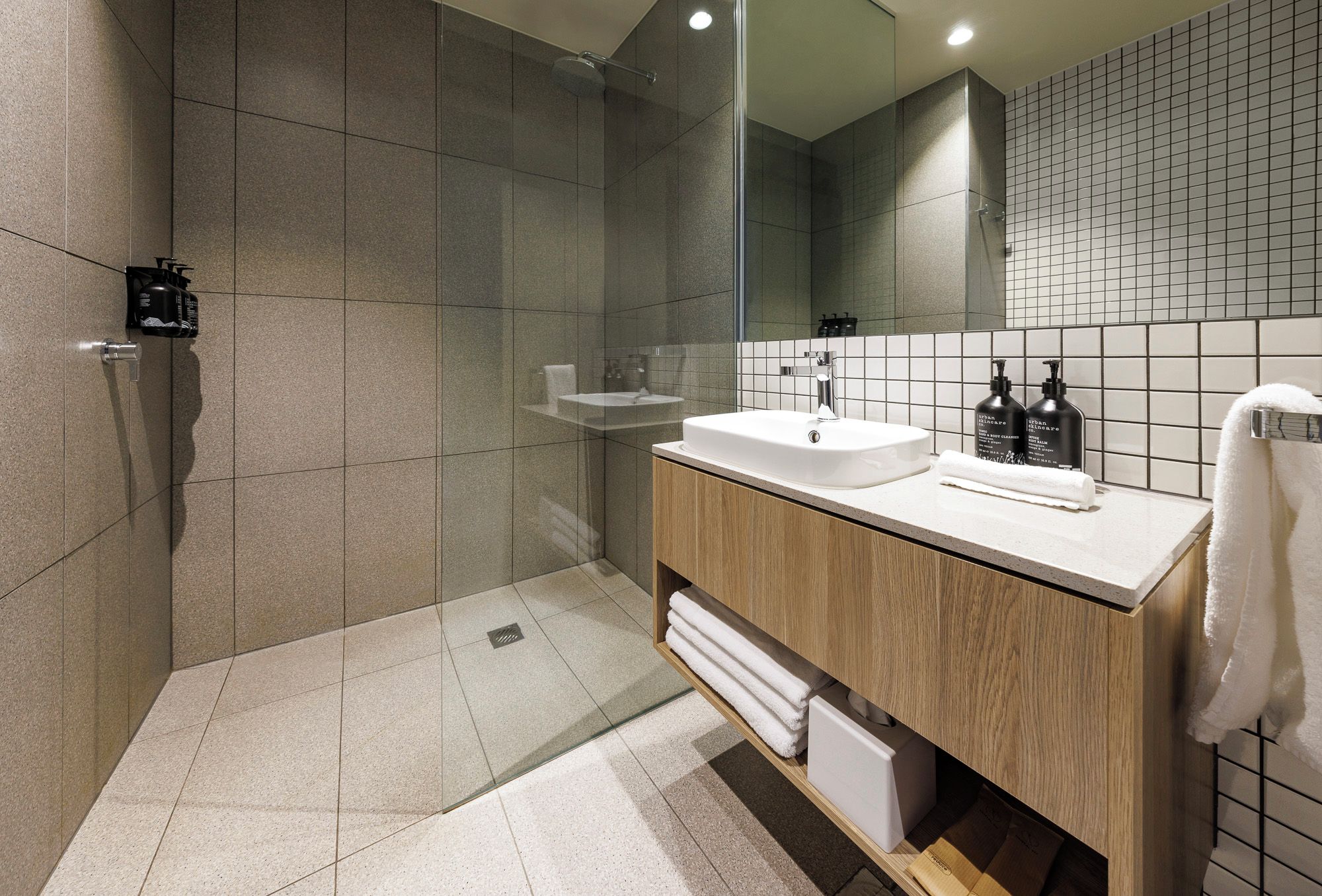 A modern bathroom with a glass shower enclosure, a white sink, and a wooden vanity.