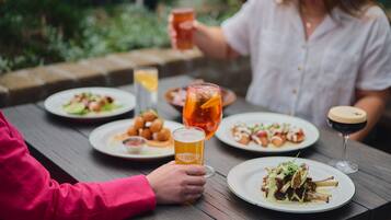 A dining table with plates of food, glasses of beer, and a wine glass.
