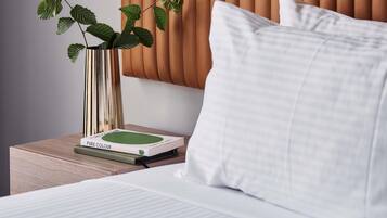 Una cama bien hecha con un almohadón blanco y un libro verde titulado 'PURE COLOUR' sobre una mesita de noche de madera.