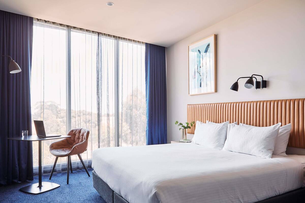 A hotel room with a large bed, a desk, a chair, and a window with curtains.