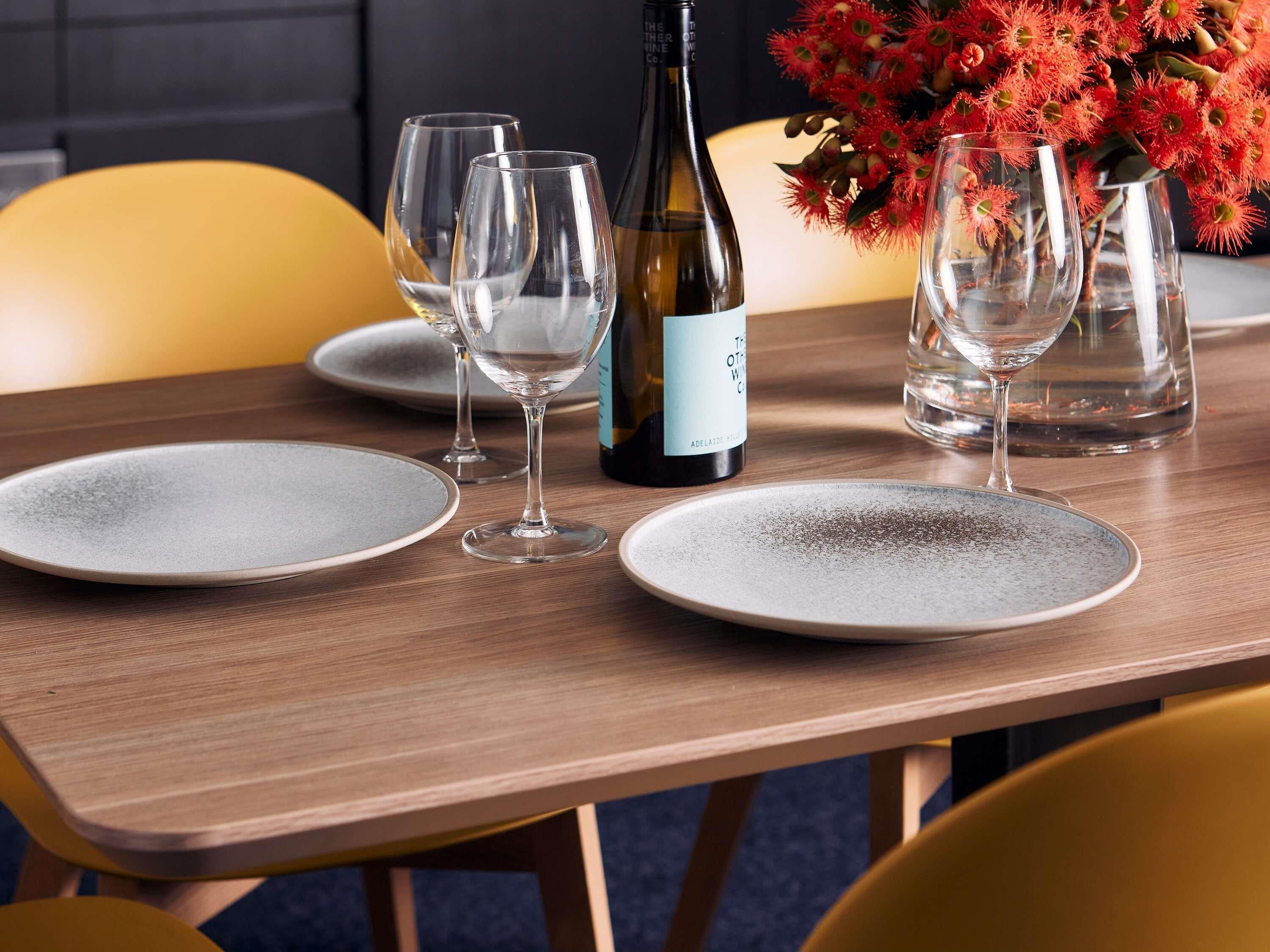 A dining table set with plates, glasses, and a wine bottle.