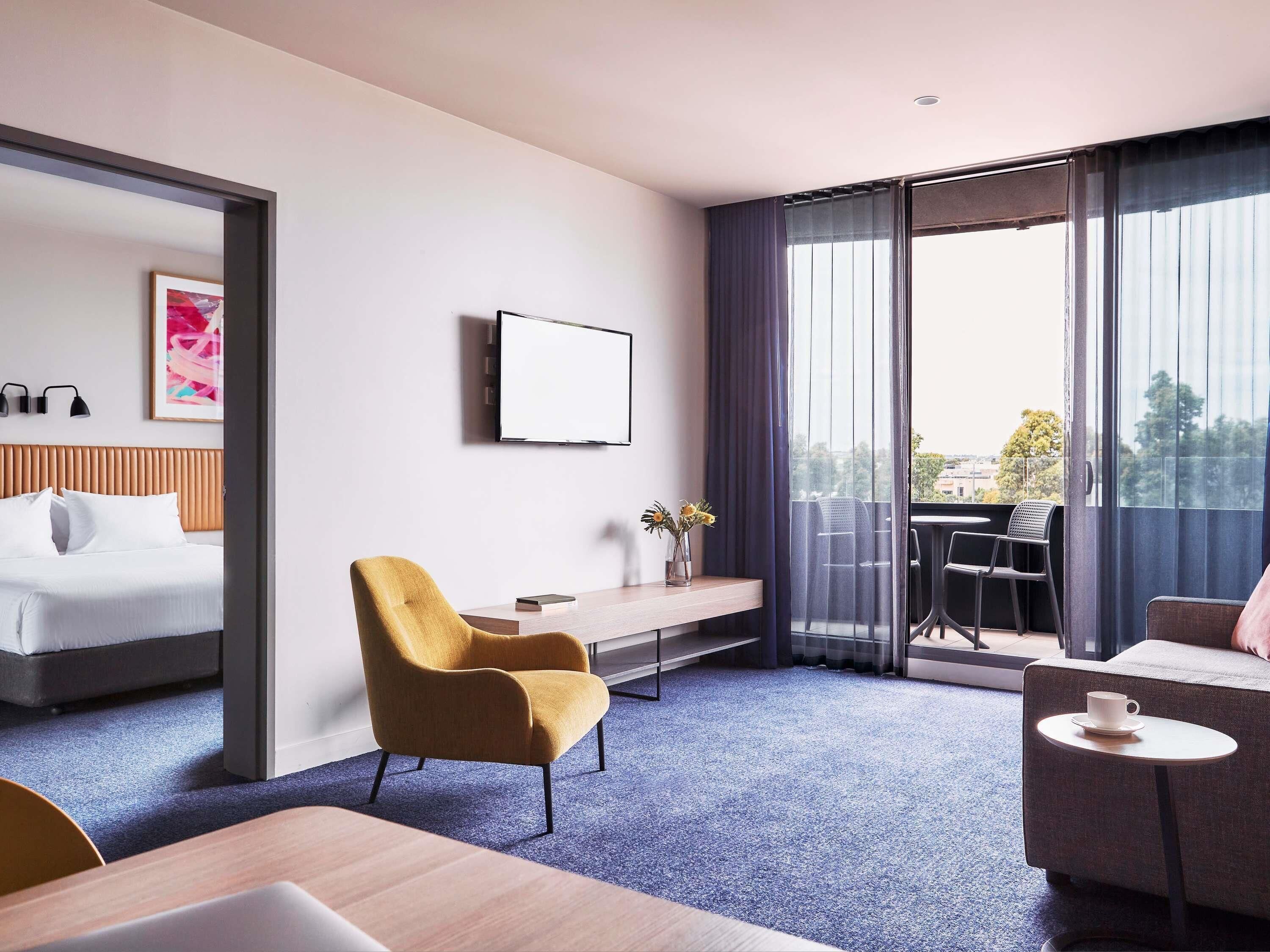 A hotel room with a bed, a desk, a chair, a small table, and a balcony with a view.