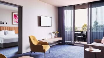 A hotel room with a bed, a desk, a chair, a small table, and a balcony with a view.