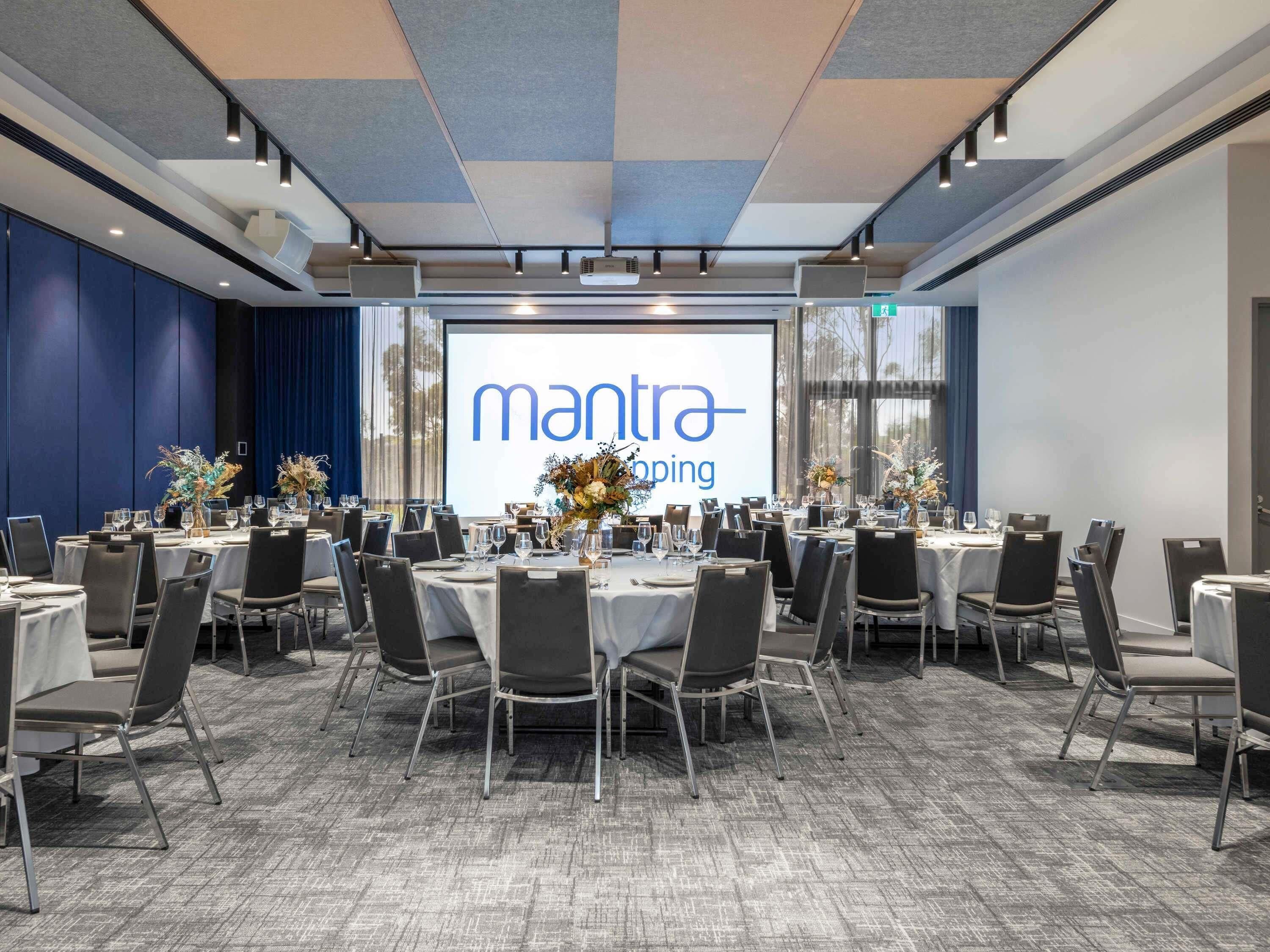 A conference room with round tables, chairs, and a large screen displaying 'mantra' branding.