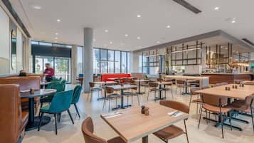 Un'ampia sala ristorante con soffitti alti, grandi finestre e diverse opzioni di posti a sedere, tra cui cabine e tavoli.