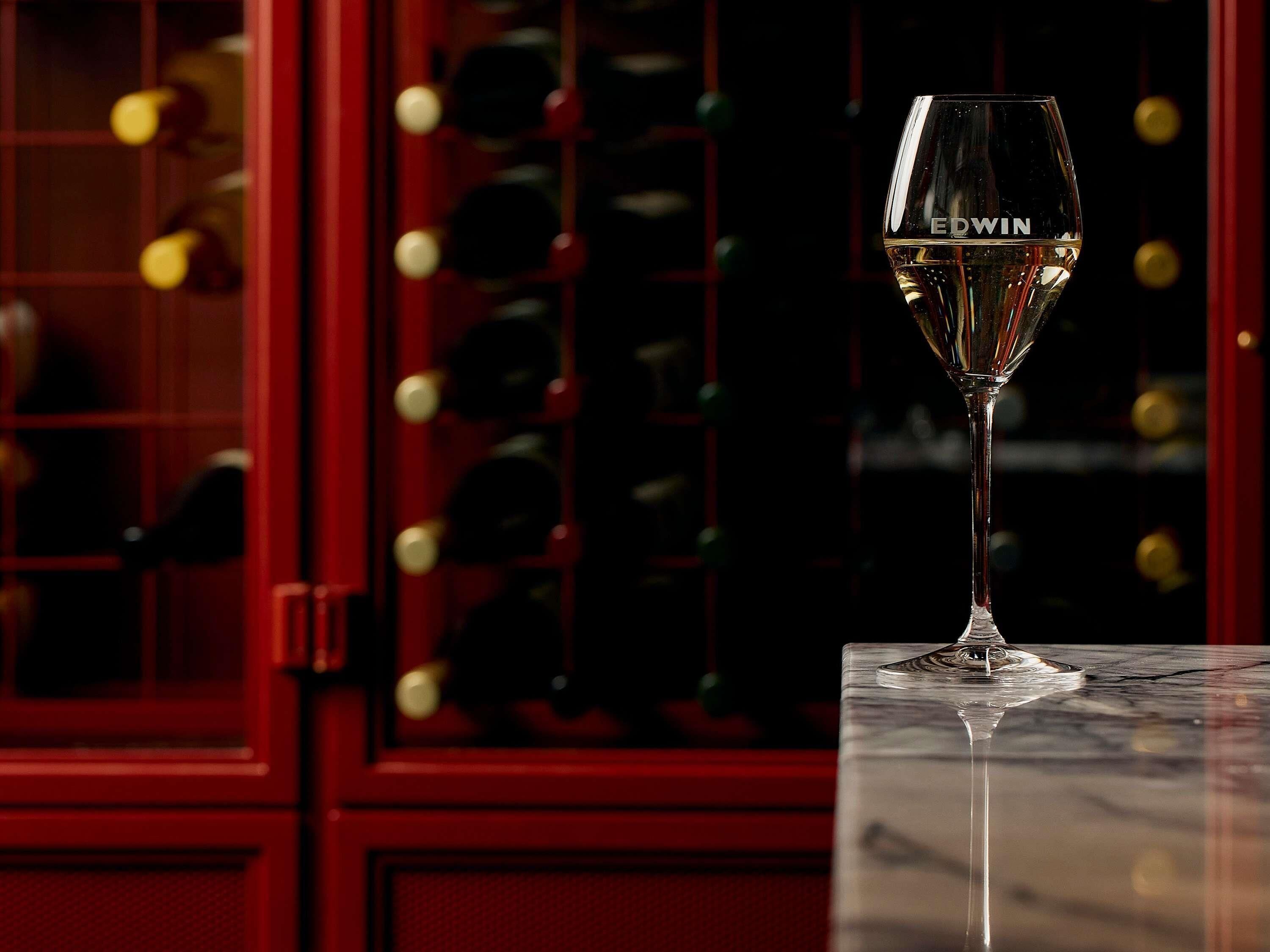 A wine glass with 'EDWIN' on it, placed on a marble surface.