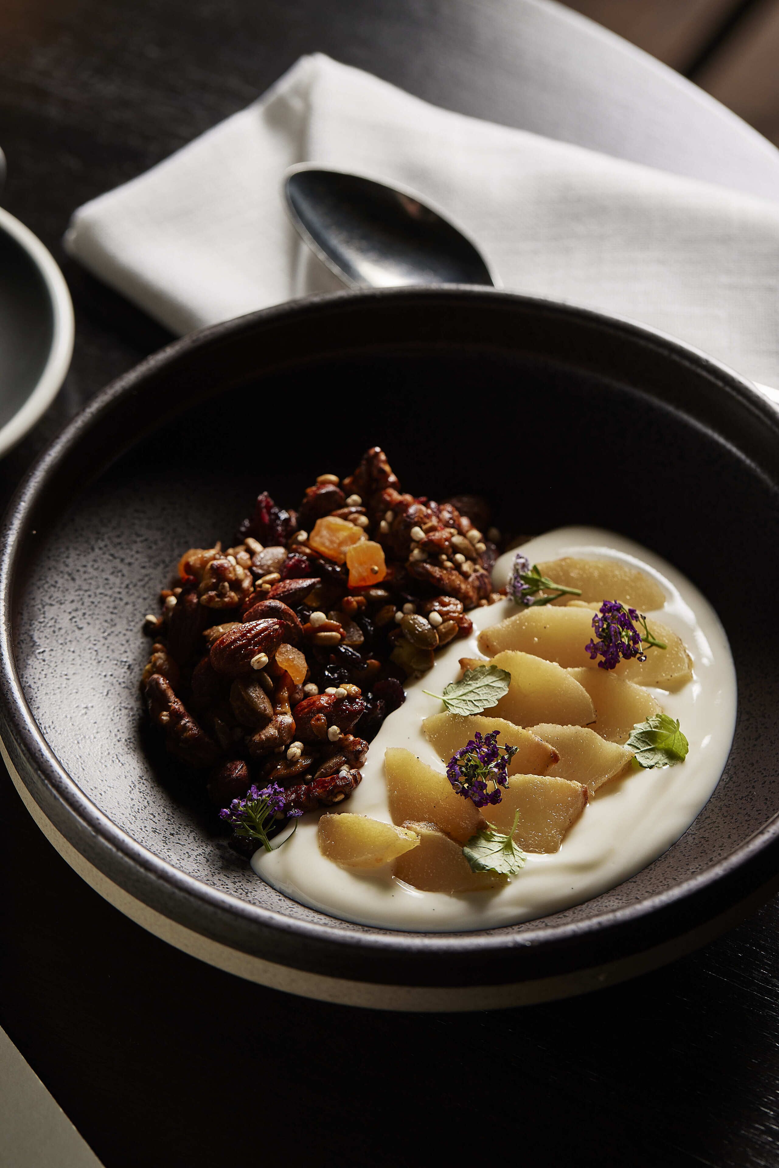 A bowl of food with nuts and dried fruits on one side and a creamy substance with potato pieces on the other.