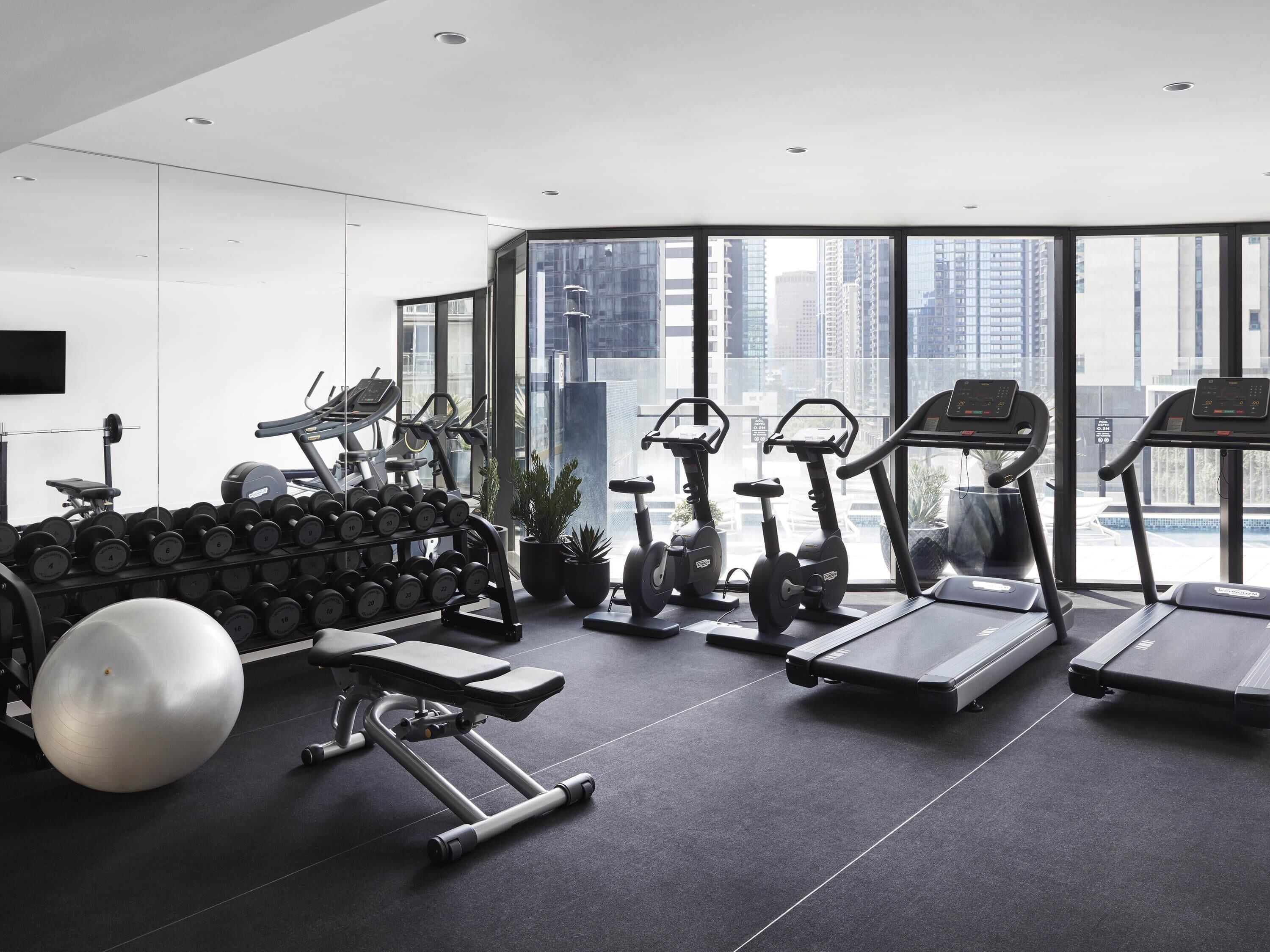 A modern gym with treadmills, elliptical machines, and a variety of dumbbells.