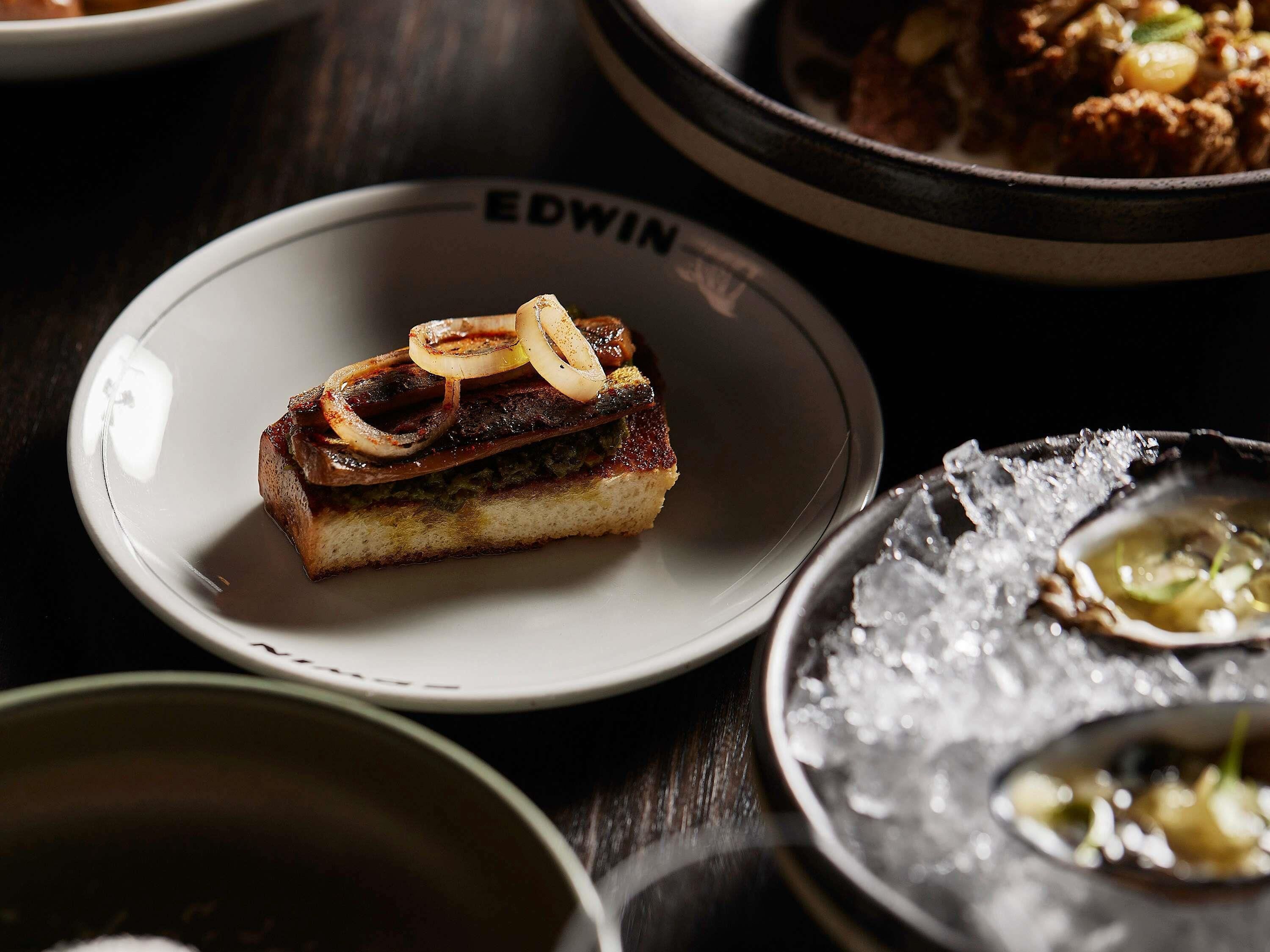 A dessert plate with a slice of cake topped with onions, a plate with the name 'EDWIN' on it, and a bowl of soup with a garnish.