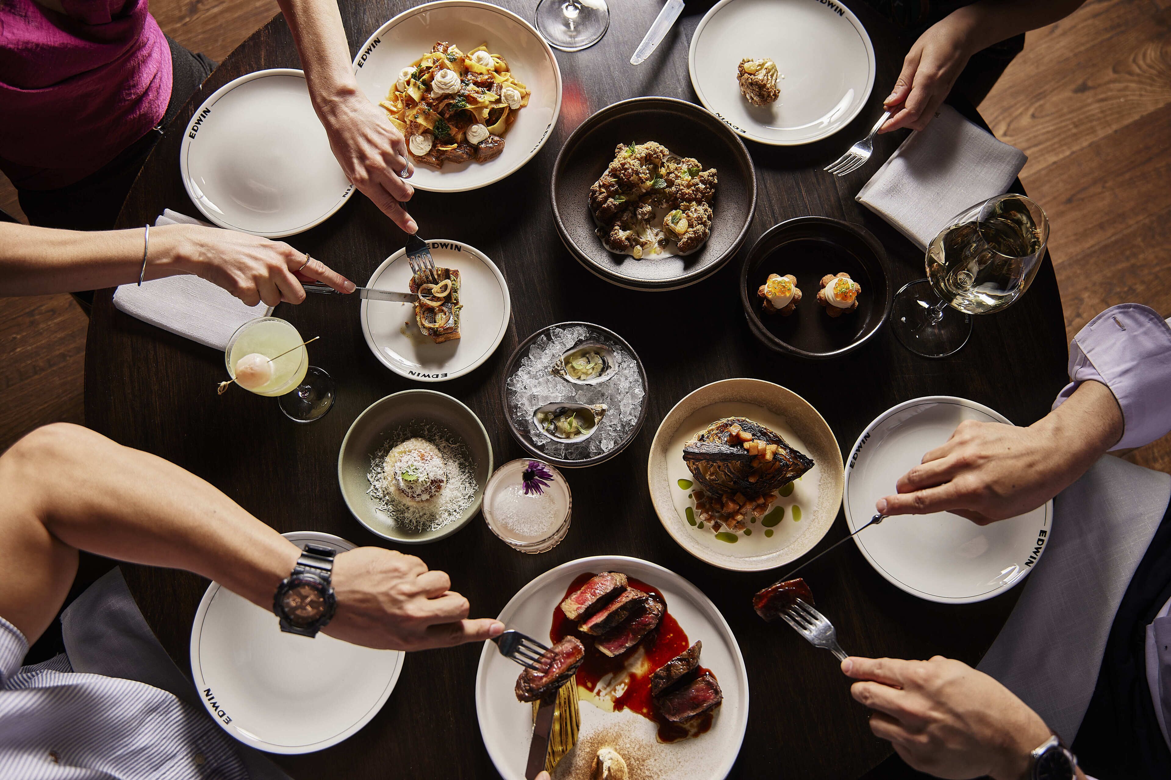 A group of people dining at a round table with various dishes and drinks.