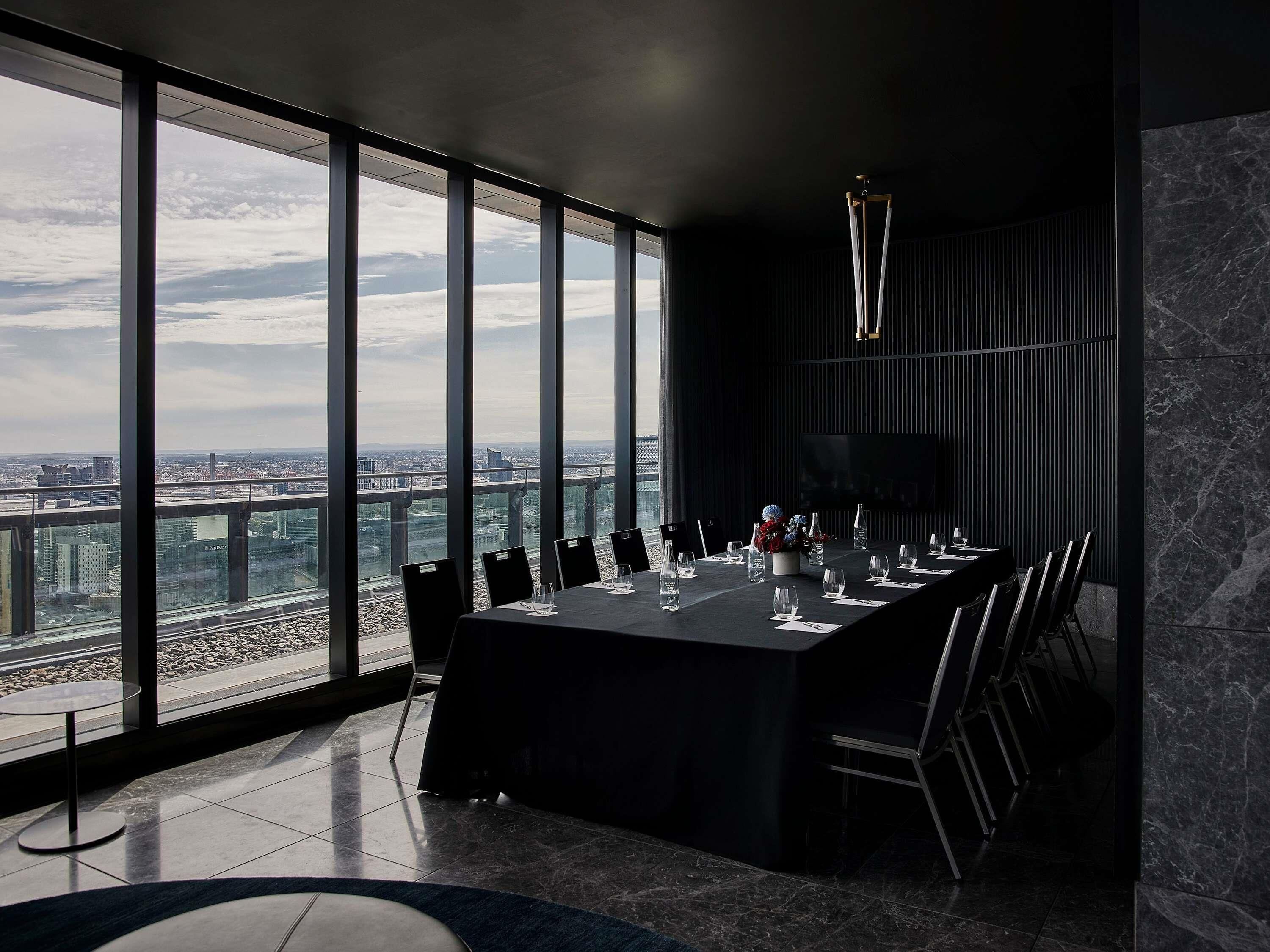 A modern conference room with a panoramic city view, a long table set for meetings, and a minimalist design.