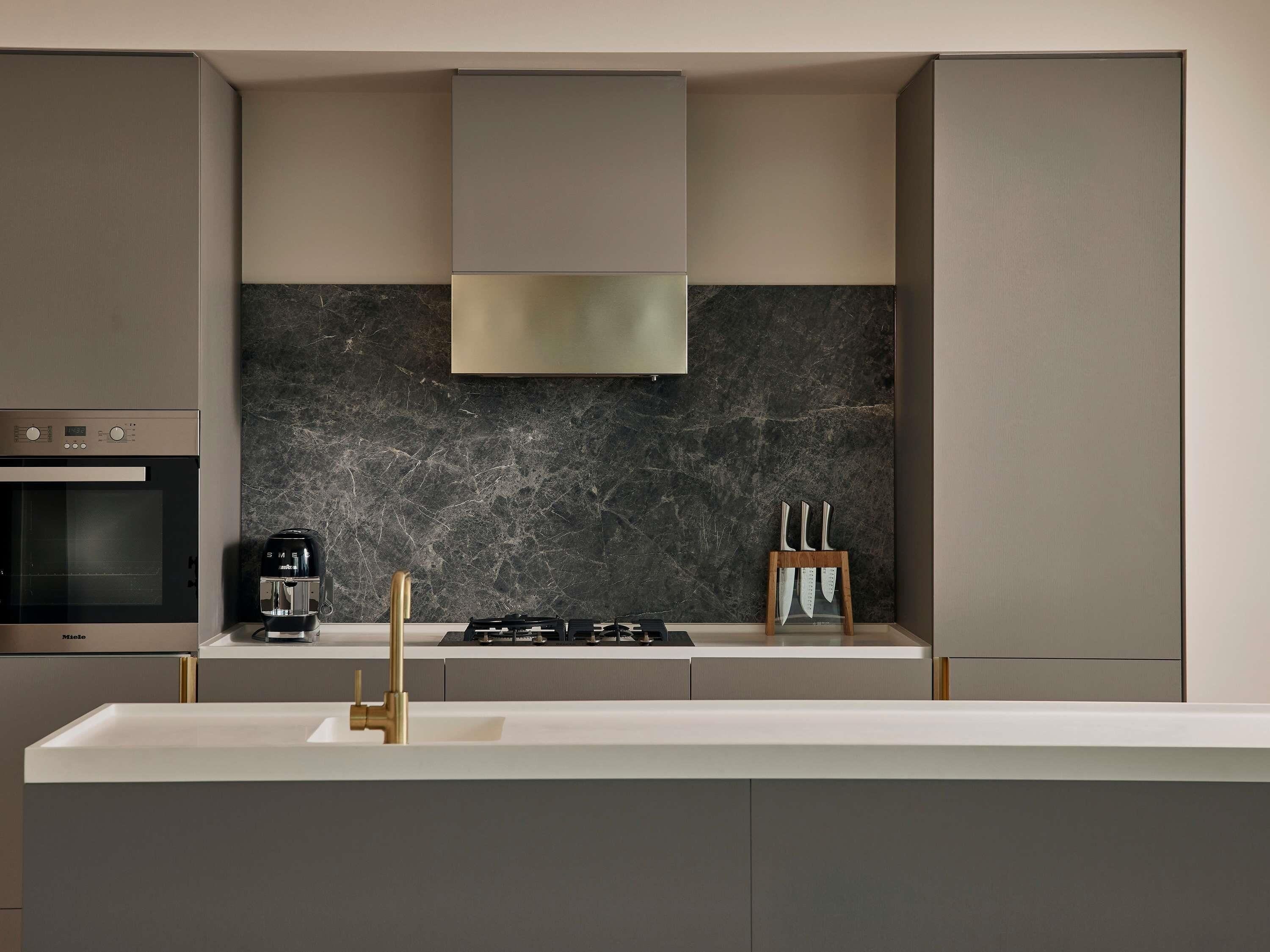 A modern kitchen with a built-in oven, a coffee machine, a gas stove, and a marble backsplash.