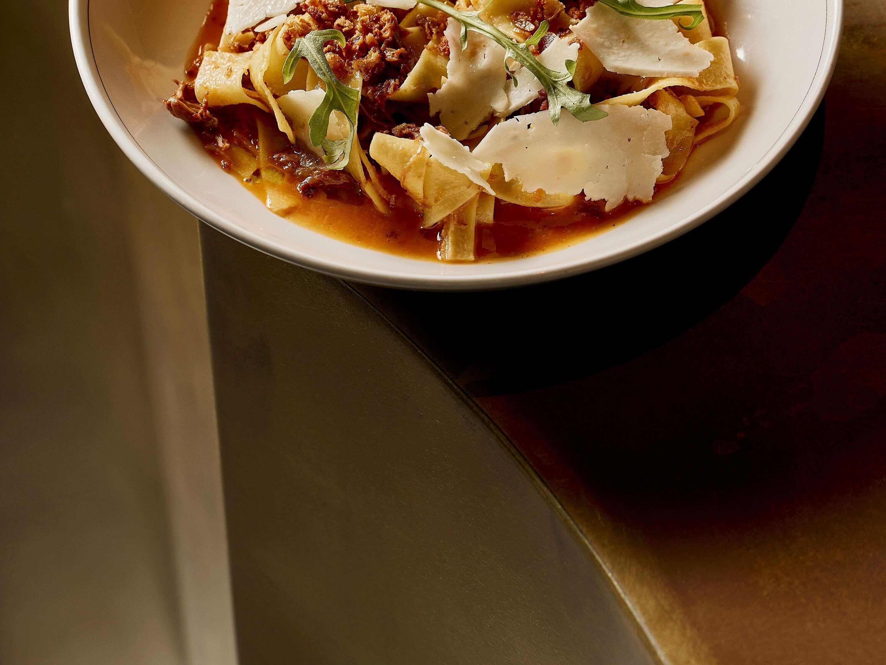 A bowl of pasta with meat and cheese garnished with greens.