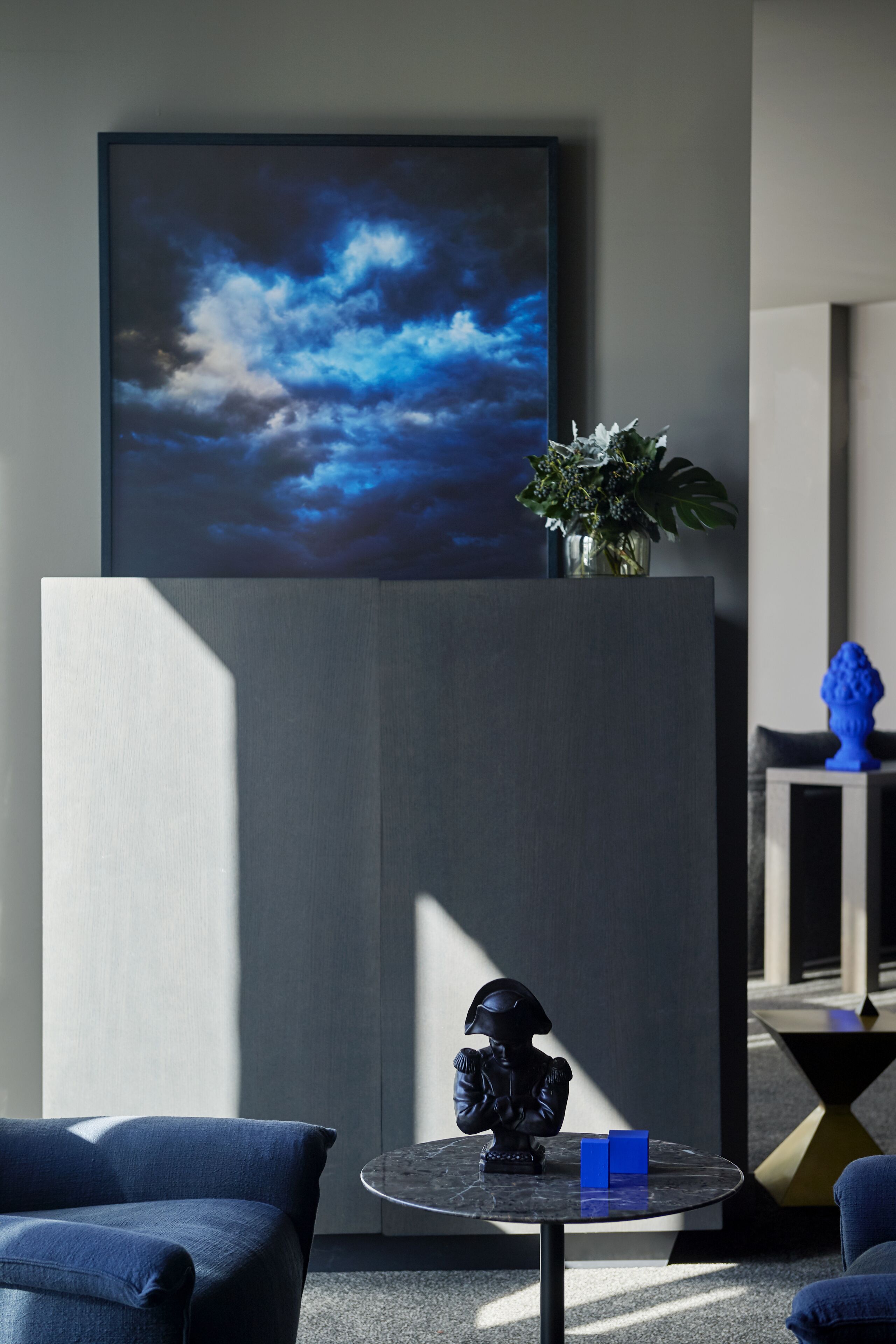Ein modernes Zimmer mit einem großen abstrakten Gemälde, einer Statue und einer Pflanzvase.