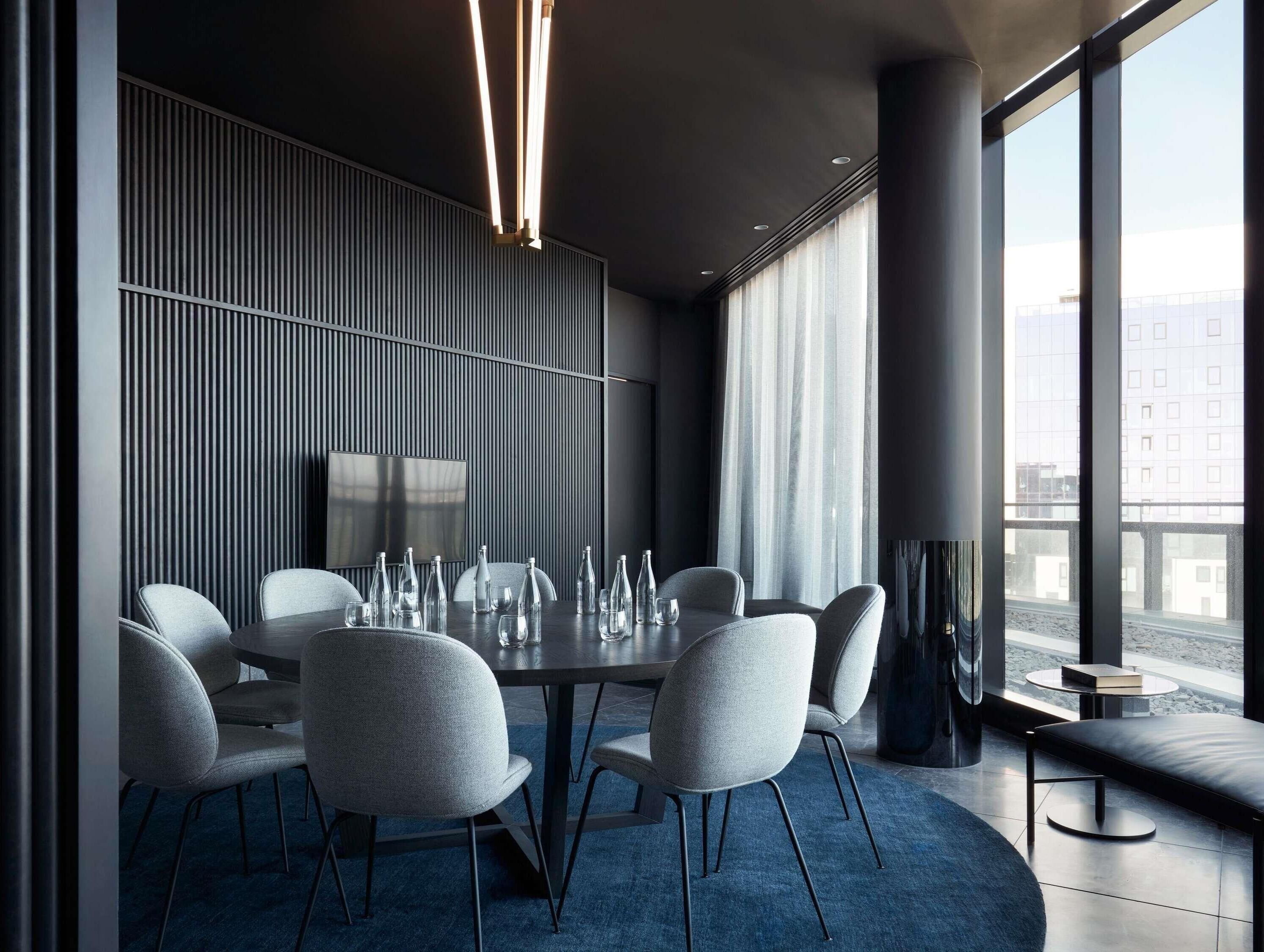 A modern conference room with a round table, grey upholstered chairs, and a large window with a city view.