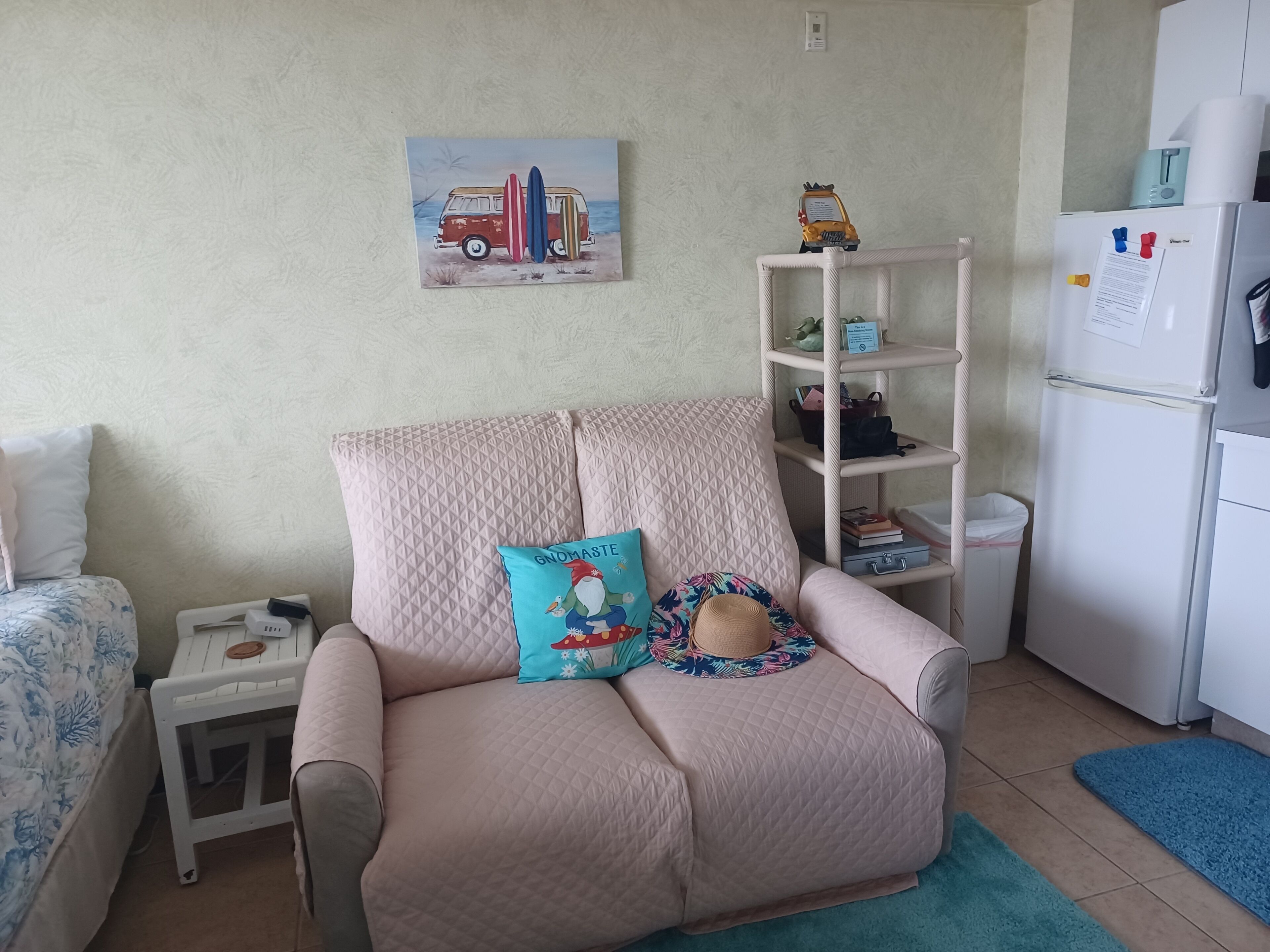 Un salon avec un fauteuil beige, une petite table, une bibliothèque et un réfrigérateur.