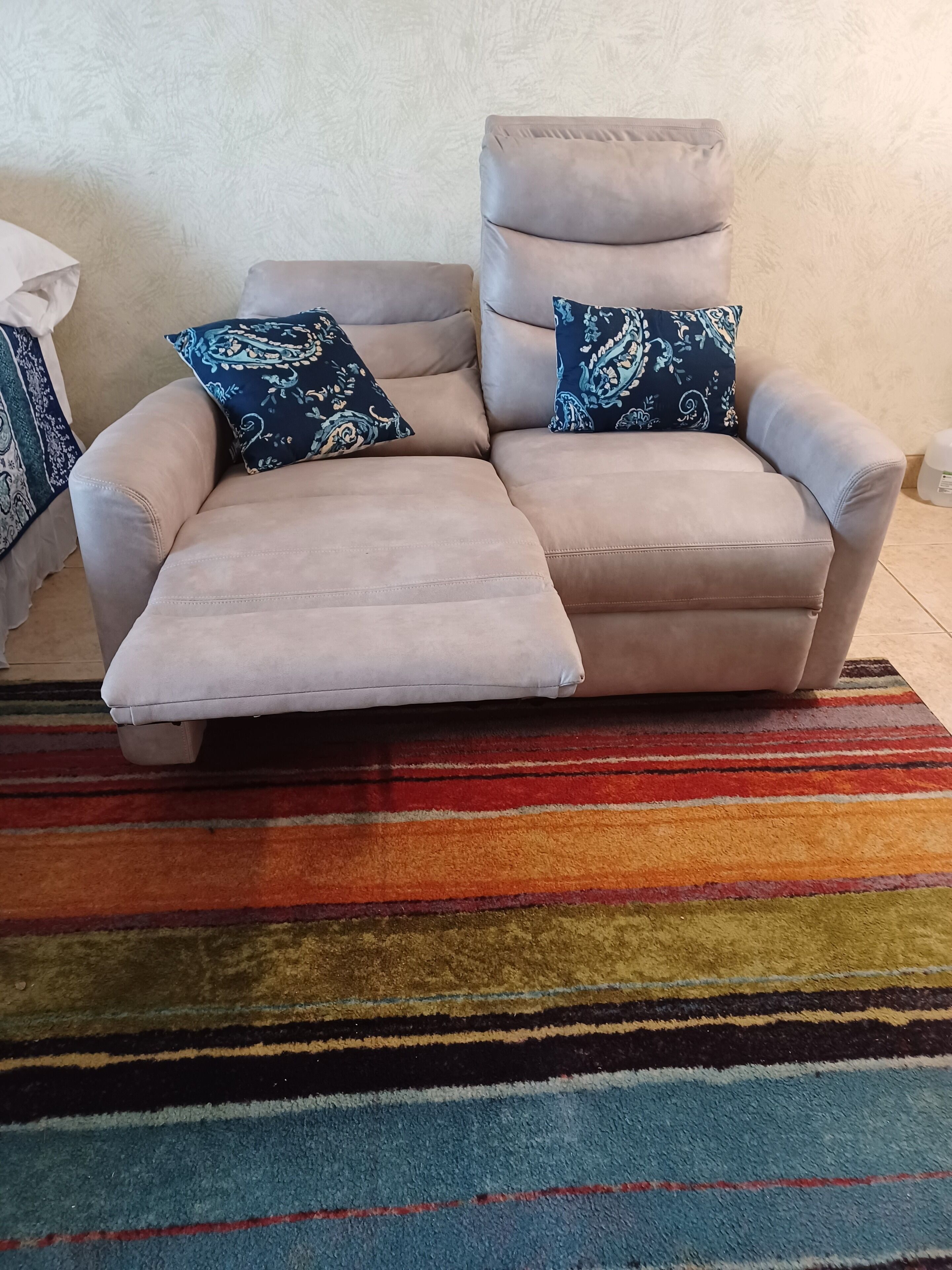 En beige fåtölj som kan lutas bakåt, med två matchande kuddar, placerad på en randig matta i flera färger.