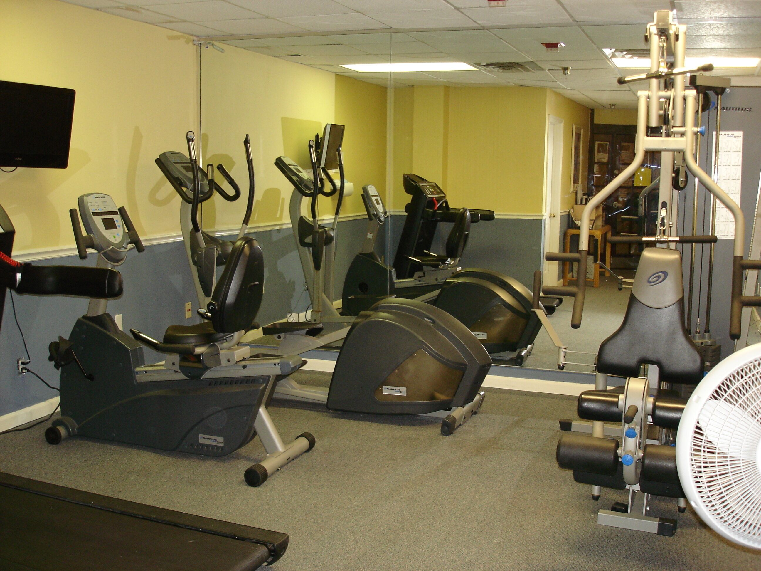 A gym with stationary bikes, elliptical machines, and a fan.