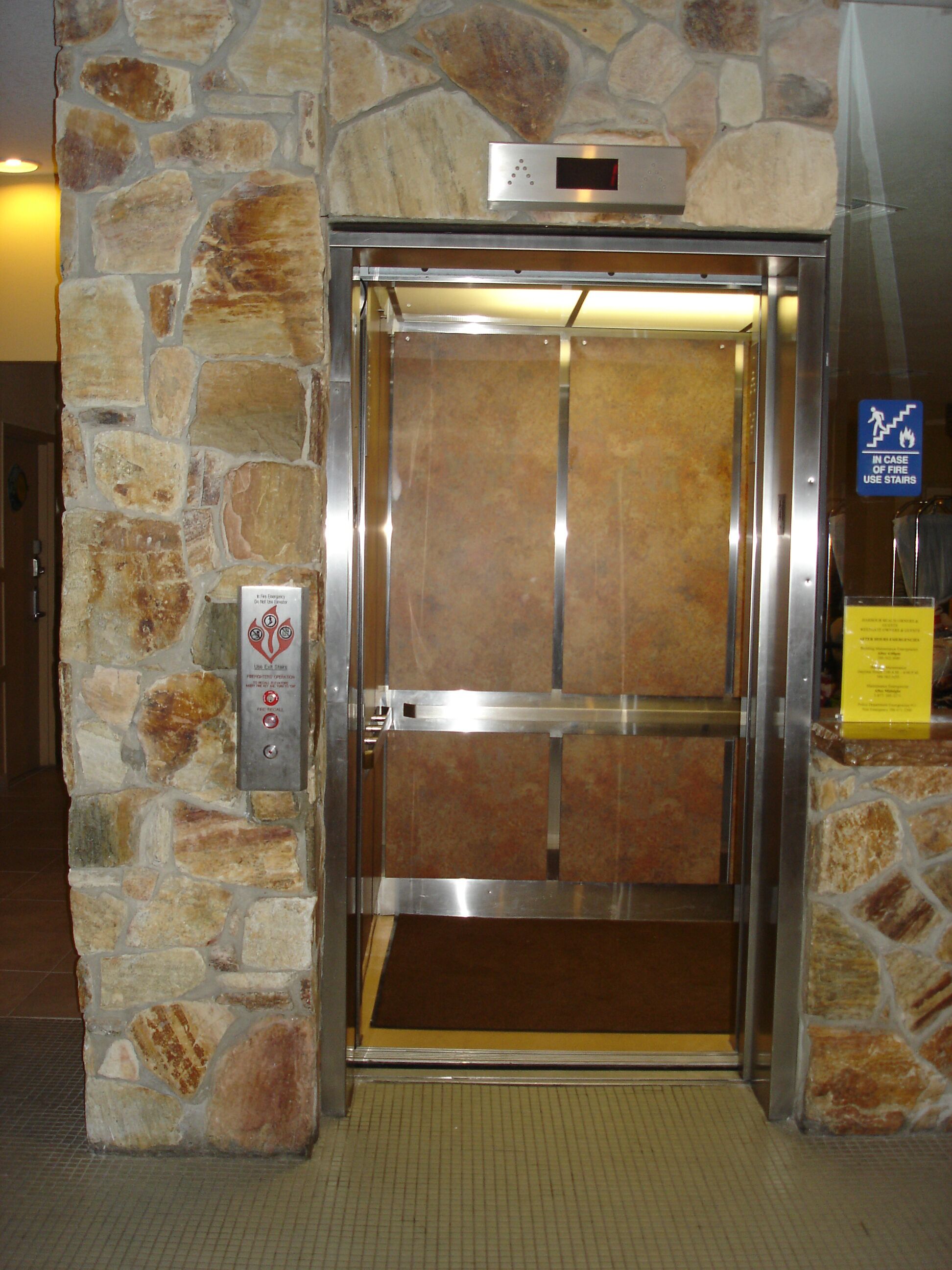 An elevator with a stone wall, a digital display, and a fire safety sign.