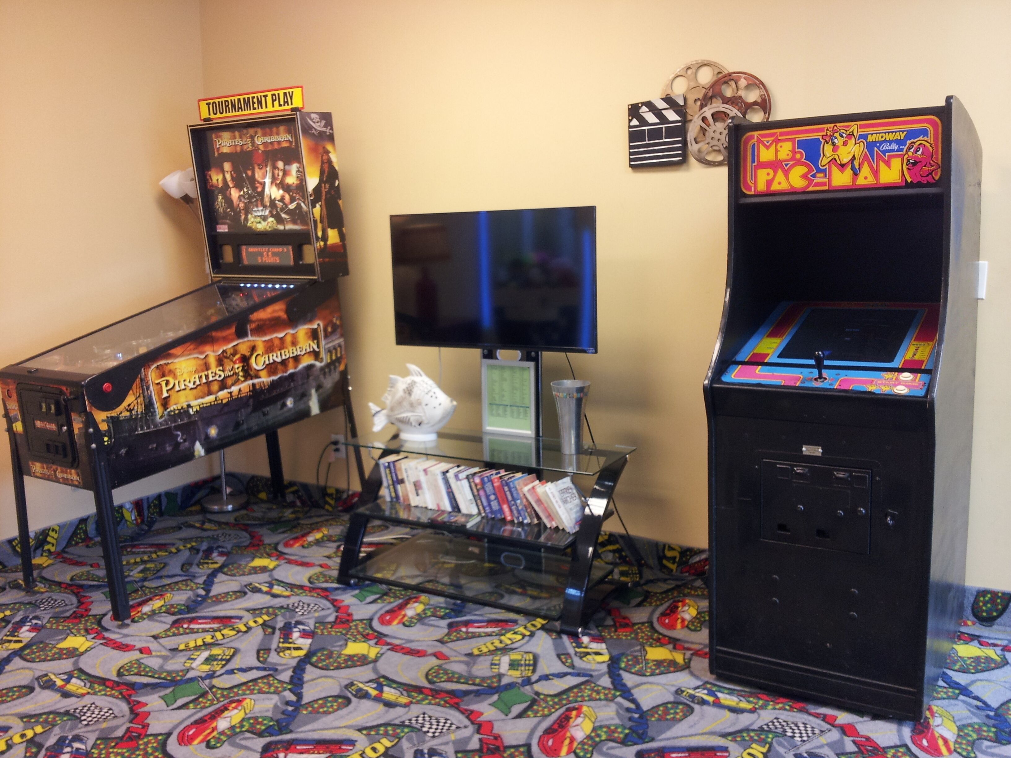 A room with two arcade machines, a television, and a glass display case with books.