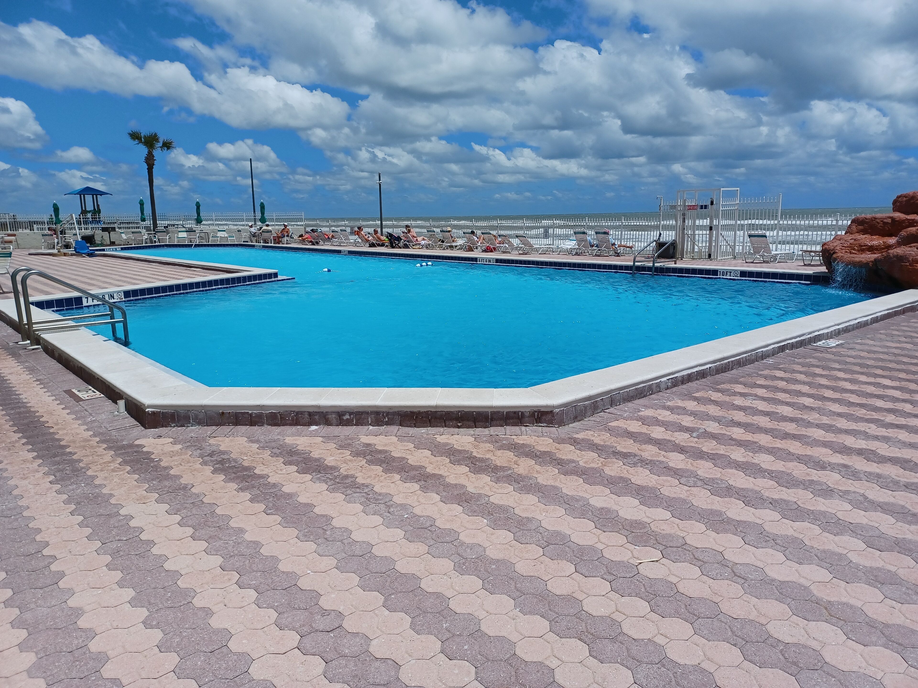 Ein Pool mit sechseckigen Fliesen, Liegestühlen und Blick auf das Meer.