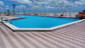 Ein Pool mit sechseckigen Fliesen, Liegestühlen und Blick auf das Meer.