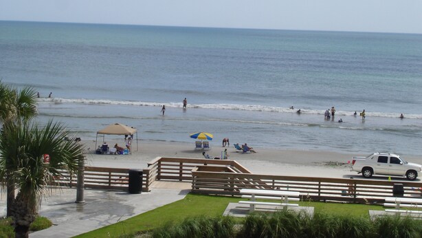 A beach with a wooden fence, picnic tables, and umbrellas. - Gorgeous Ocean View & Heated Pool! Seasonal Discounts (Daytona Beach)