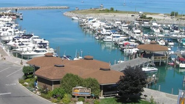 Un puerto deportivo con barcos amarrados, una carretera con vehículos y un edificio con un letrero.