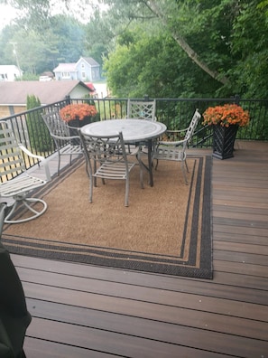 Eine Holzterrasse mit einem runden Tisch und Stühlen, umgeben von einem Metallgeländer und Blumentöpfen.