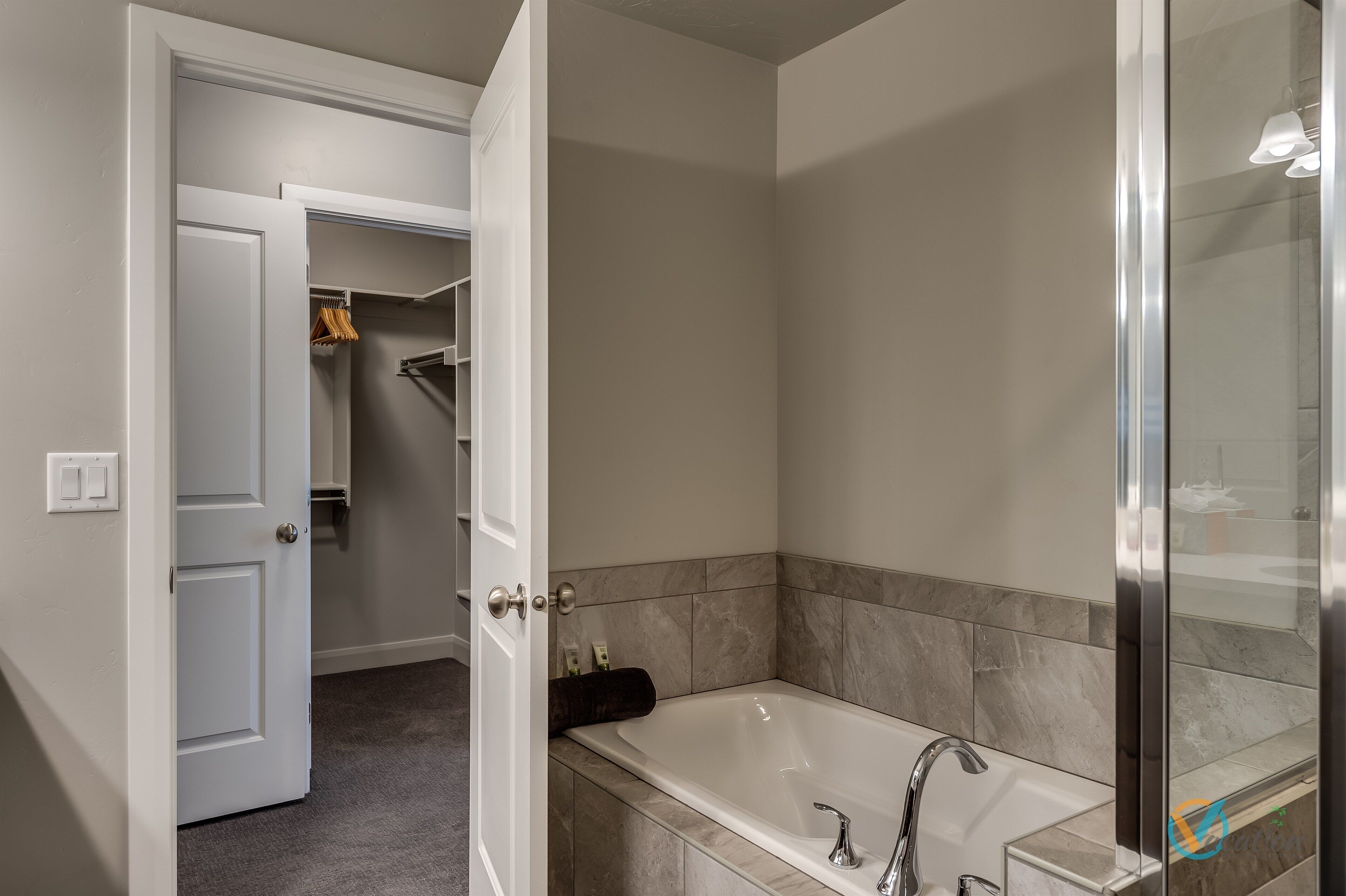 A modern bathroom with a freestanding bathtub, a glass shower enclosure, and a walk-in closet with hanging clothes.