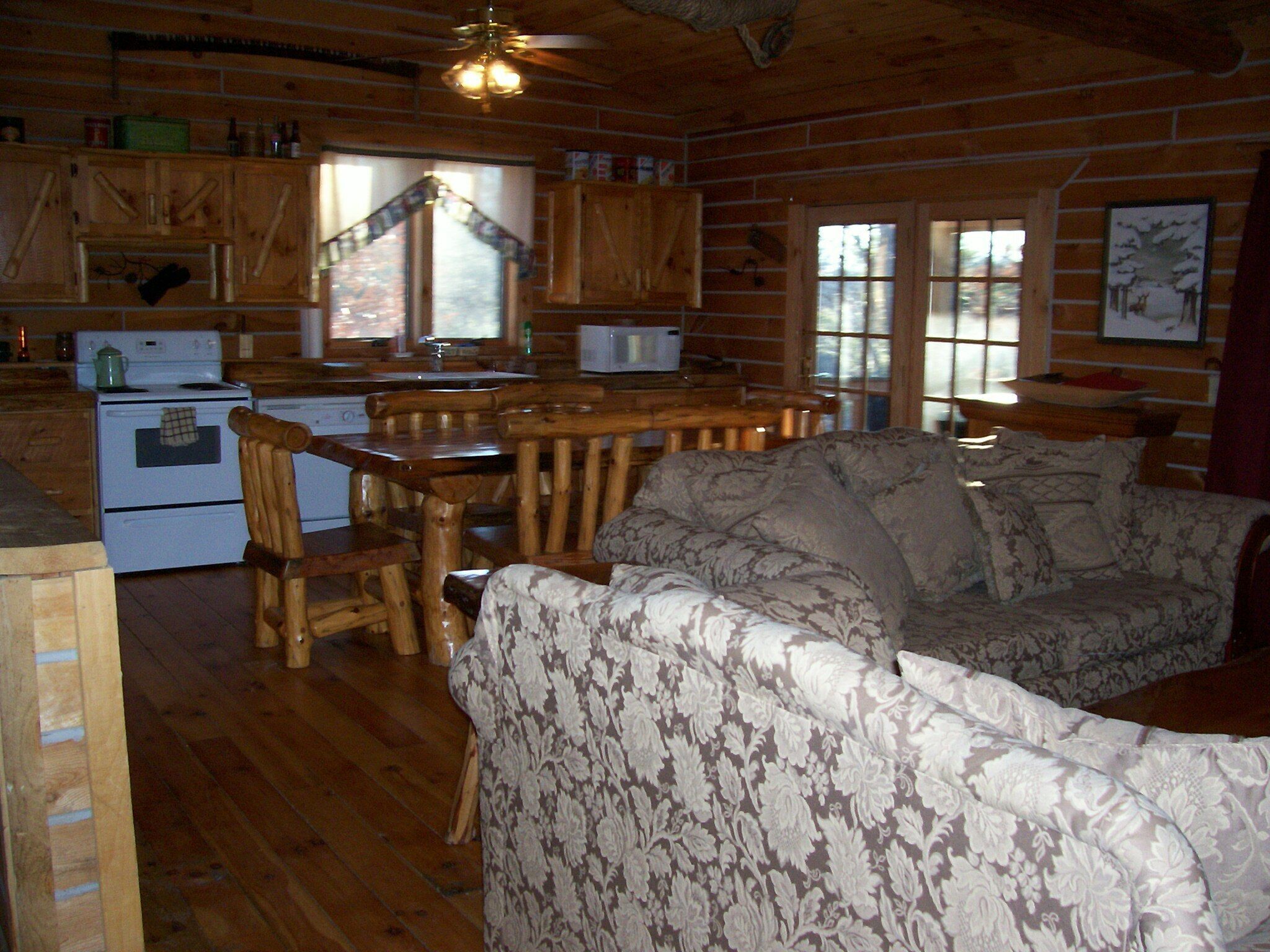 Ein gemütliches Blockhaus-Interieur mit einem Holzesstisch, einer Couch, einer Küchenzeile mit Herd und Schränken sowie einem Fenster mit Aussicht.
