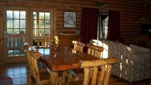 Interior de una cabaña de madera con una mesa de comedor, sillas, un sofá y una chimenea.
