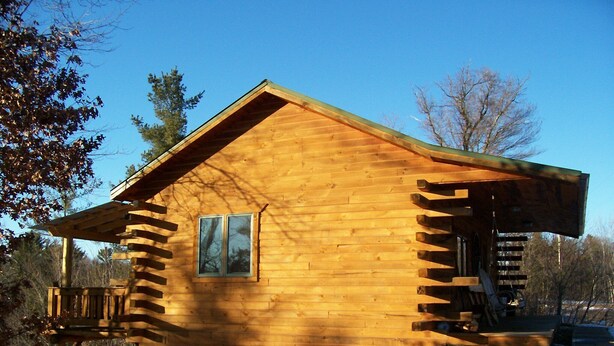Una cabaña de madera con ventana, un porche y una escalera que sube a una terraza.