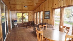 A wooden cabin with a dining area, a sofa, and large windows. - Turtle Lake Retreat: Spacious Seven-Bedroom Home -  Your Ultimate Group Getaway! (Deerwood)