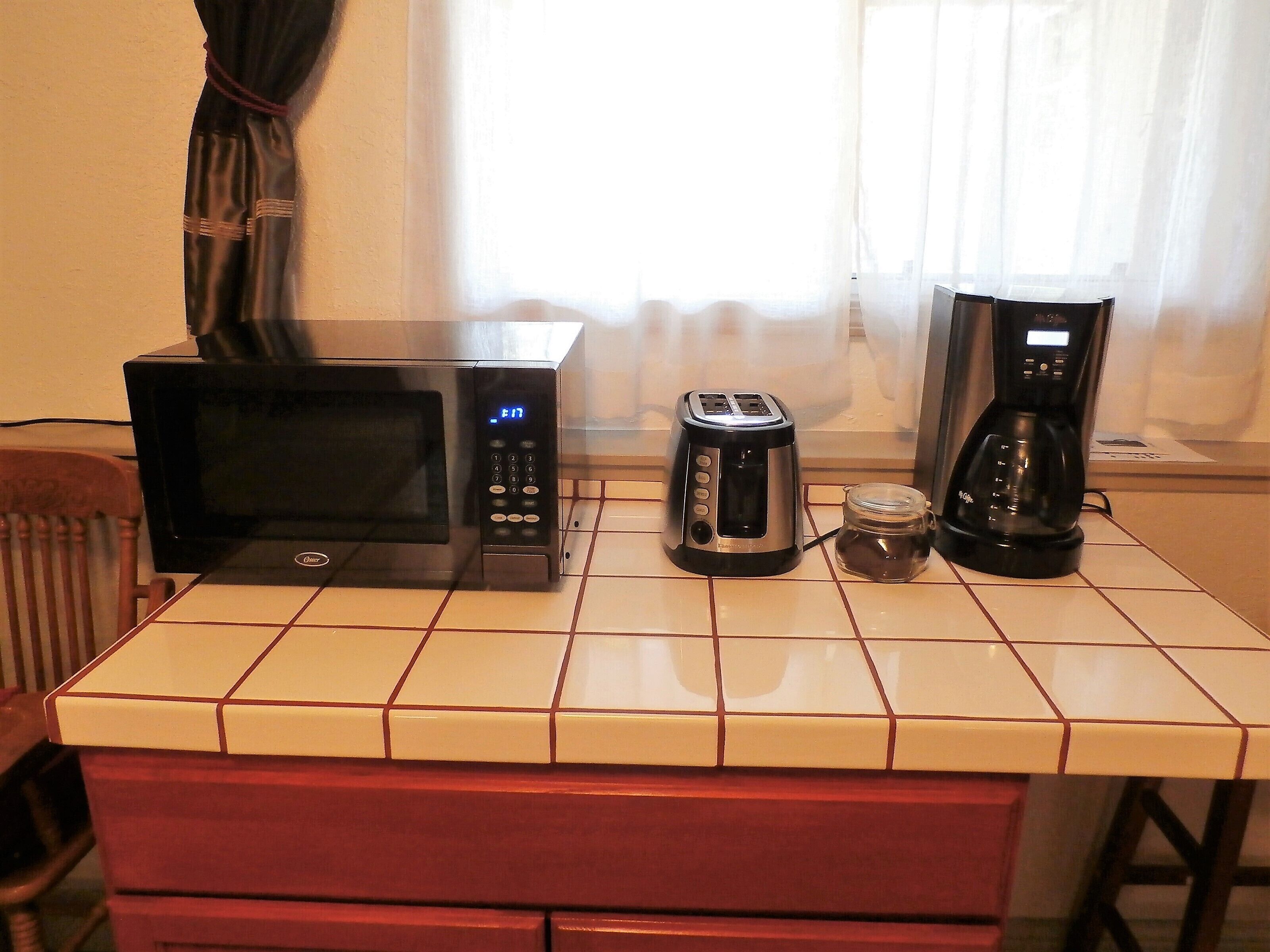 A kitchen with a microwave, toaster, and coffee maker on a tiled countertop.