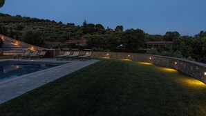 Uma área de piscina com muro de pedra, gramado e algumas cadeiras de descanso.