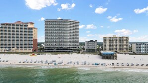 Un hôtel en bord de mer composé de plusieurs immeubles de grande hauteur, une plage de sable avec des parasols et une jetée qui s’avance dans l’eau.