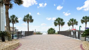 Un chemin pavé bordé de palmiers, une clôture et une vue sur la plage.