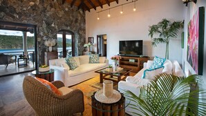 A spacious living area with a stone wall, wooden ceiling, and a large flat-screen TV. There are multiple seating arrangements including a sofa, chairs, and a coffee table. - Blackbeard's Hideaway at Steele Point (West End)