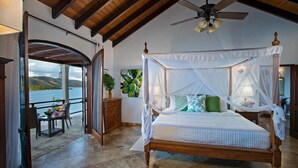 A bedroom with a four-poster bed, a ceiling fan, and a view of the sea. - Blackbeard's Hideaway at Steele Point (West End)