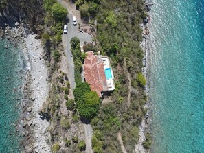 An aerial view of a coastal property with a swimming pool, a paved driveway, and a rocky shoreline. - Blackbeard's Hideaway at Steele Point (West End)