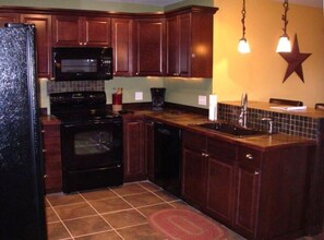 Kitchen area with a sink, oven, microwave, and refrigerator, featuring a tiled backsplash and island.