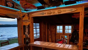 A wooden cabin with a view of a lake, featuring a bar area with a sign for 'Twisted Tea' and a 'True Iced Tea Taste' sign.