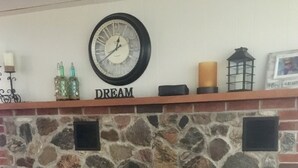 A stone fireplace with a clock above it and a shelf with decorative items.