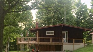 A two-story cabin with a deck, surrounded by trees.